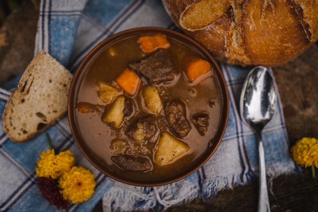 Beef stew with carrots and potatoes in brown ceramic bowl, served with bread