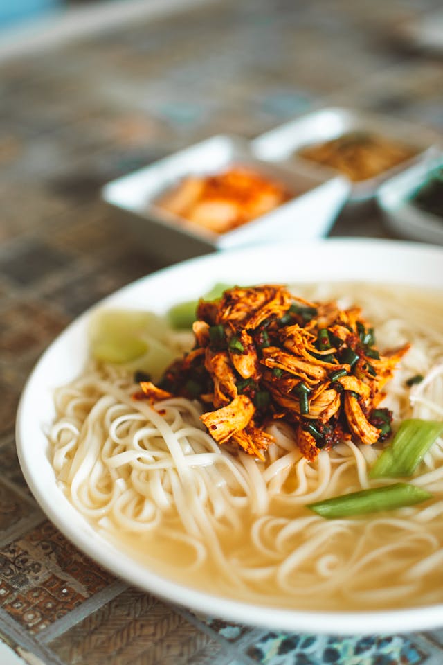 Fresh ingredients for chicken noodle soup - carrots, celery, garlic, herbs, and egg noodles on wooden cutting board