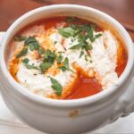 Creamy tomato soup in a white bowl with golden grilled cheese dippers on the side, fresh basil garnish on top