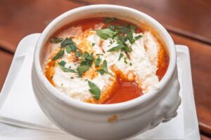 Creamy tomato soup in a white bowl with golden grilled cheese dippers on the side, fresh basil garnish on top