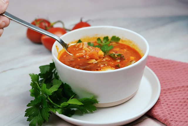 Bowl of creamy homemade tomato soup with a spoon, fresh cherry tomatoes and basil leaves around the bowl