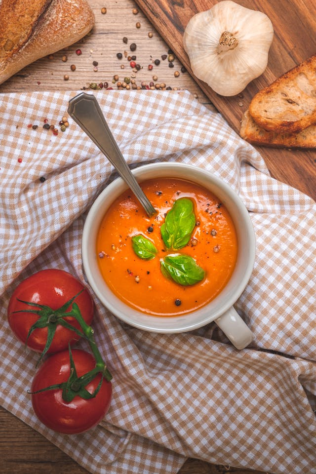 Top view of creamy tomato soup in a white ceramic bowl surrounded by fresh tomatoes, basil, and grilled cheese strips