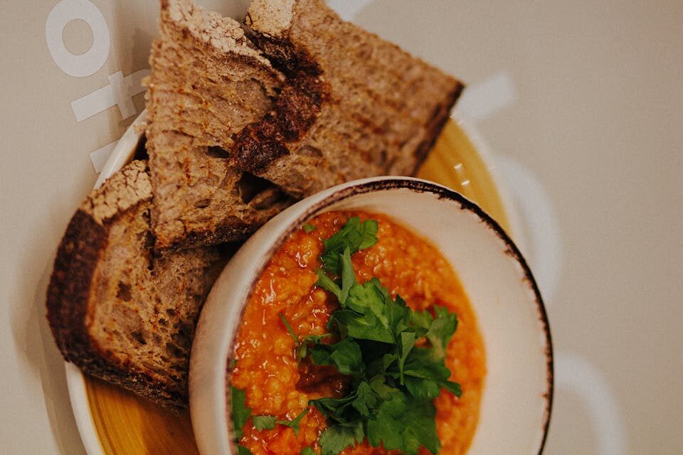 Bowl of hearty lentil soup with sausage and kale, served with crusty rustic bread on wooden table - cozy comfort food