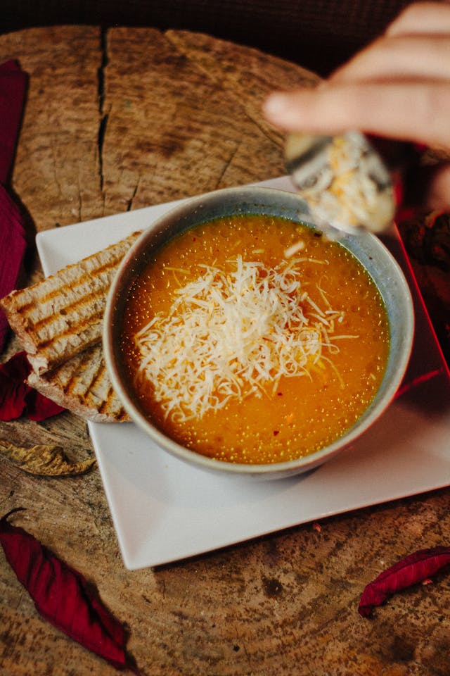 Creamy tomato soup topped with melted cheese in a white bowl, grilled cheese bread strips on the side for dipping