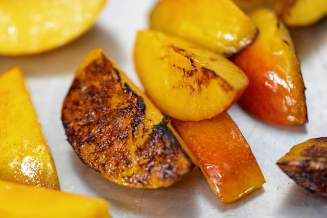 Fresh peaches grilling on BBQ with golden grill marks - caramelized summer fruit