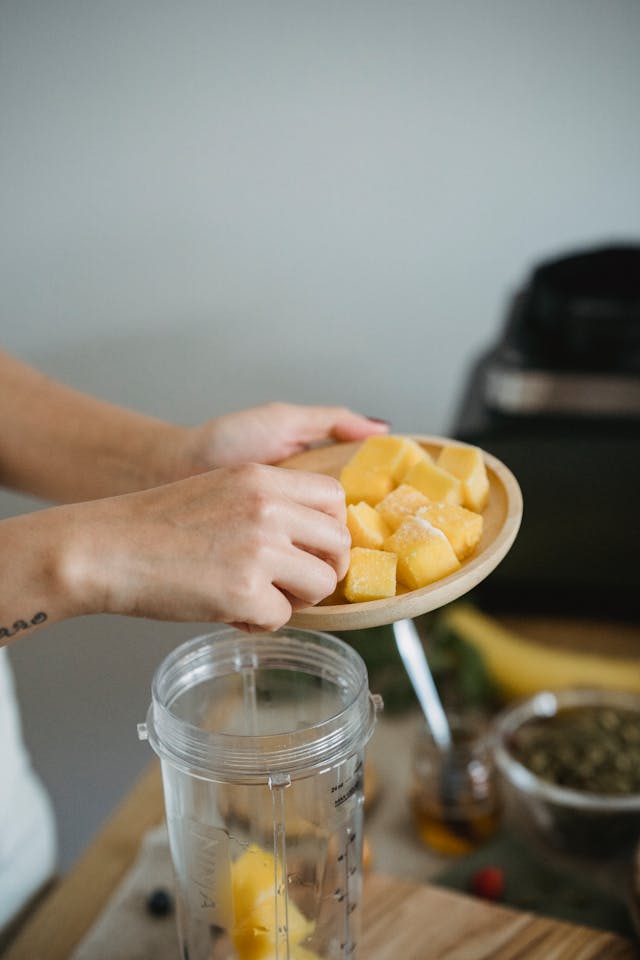 Fresh ingredients for mango date smoothie - mango slices, Medjool dates, and plant-based milk next to blender
