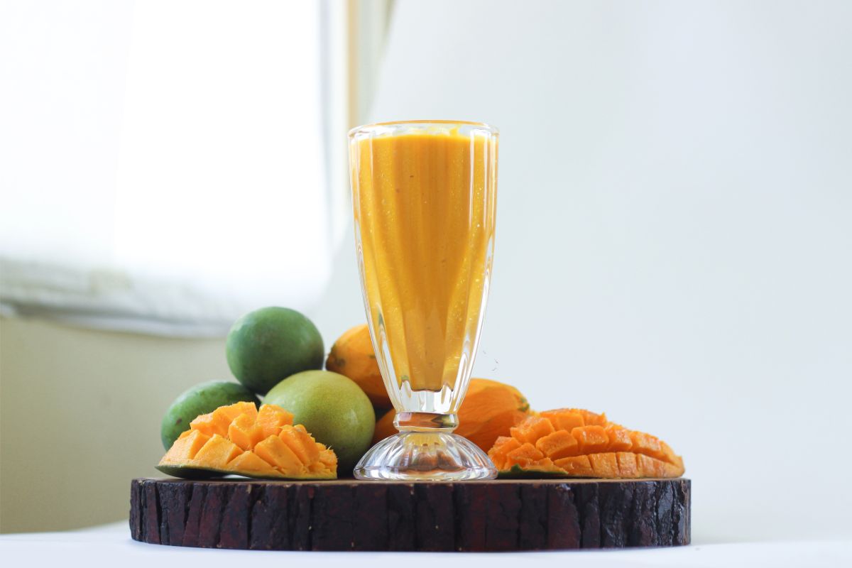 	Mango date smoothie served in glass with mango chunks and mint garnish on wooden table