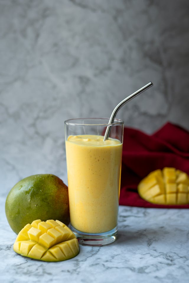 Mango lassi poured into glasses with ice cubes on side
