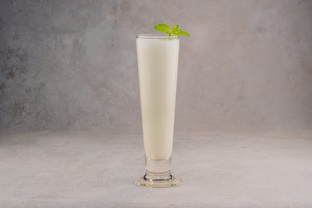 creamy sweet lassi in a glass topped with froth