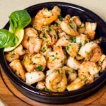 Easy homemade shrimp scampi in a cast iron skillet, featuring juicy shrimp, garlic, lemon slices, and fresh herbs.