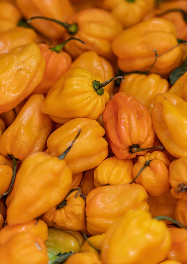Fresh orange habanero peppers on a wooden cutting board beside a jar of hot honey sauce