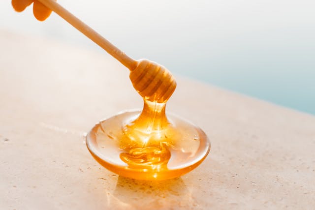 Raw wildflower honey dripping from a wooden dipper into a bowl of spicy BBQ sauce