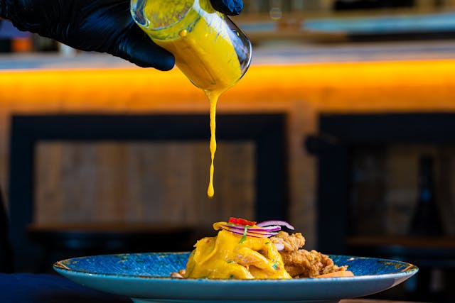 Raw wildflower honey dripping from a wooden dipper into a bowl of spicy BBQ sauce