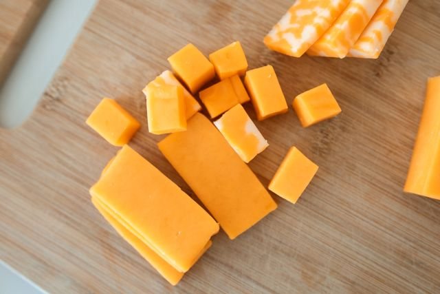 Freshly shredded sharp cheddar cheese on a cutting board for broccoli cheddar soup